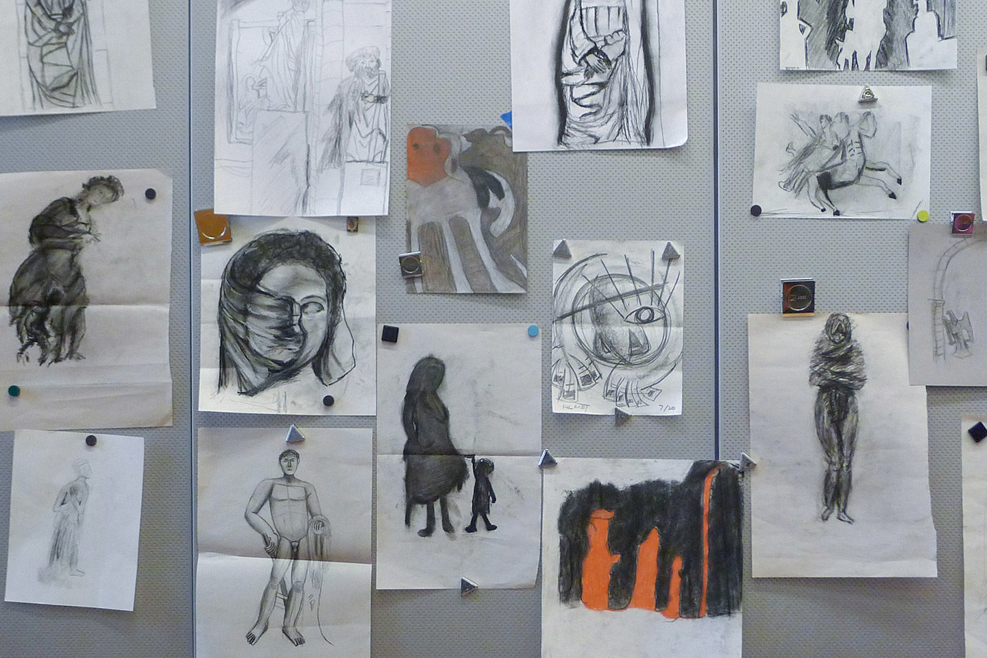 Pinned charcoal drawings of assorted artworks fill up a grey board wall-space